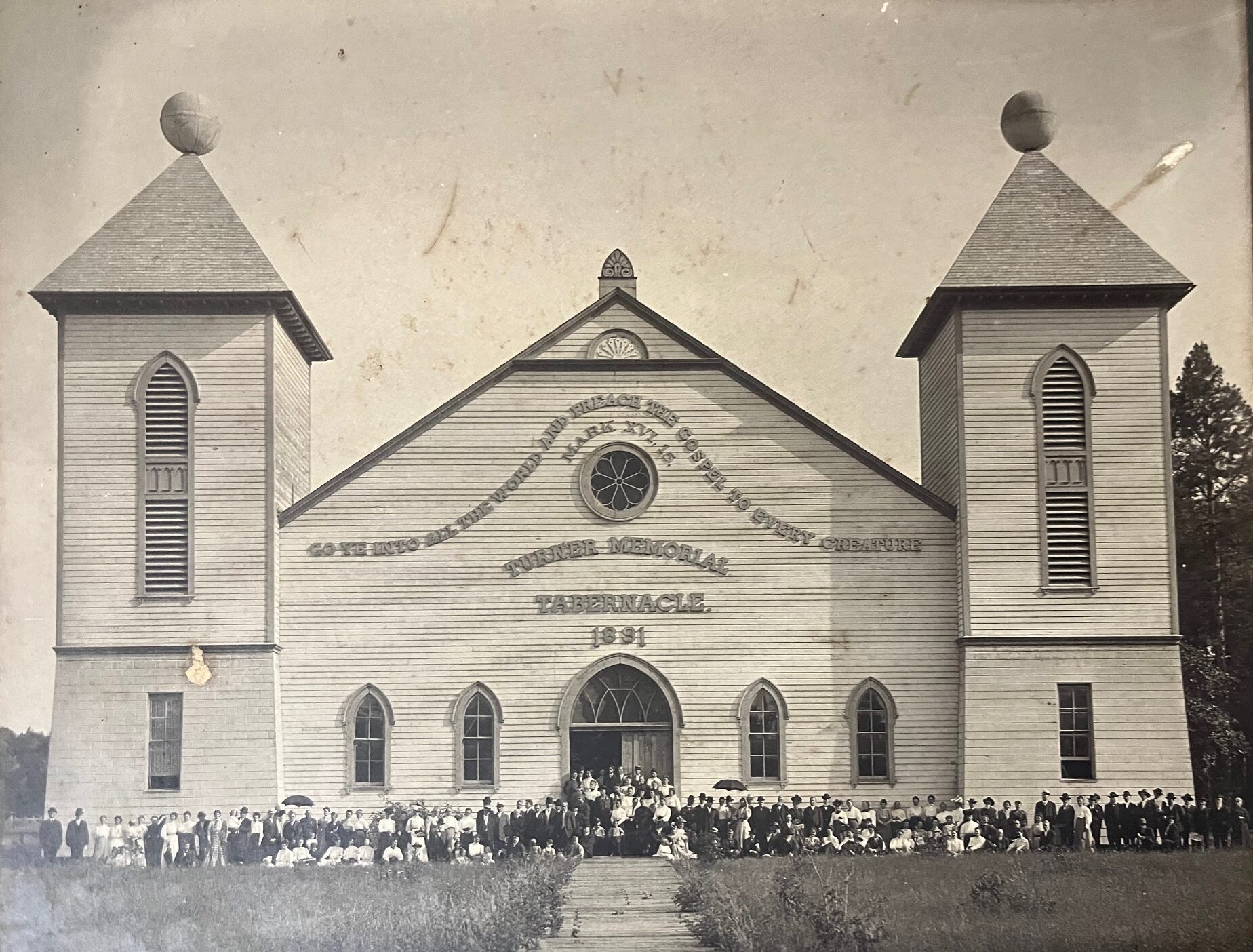 A large congregation sitting outside a church, the black and white photograph is browned with age.